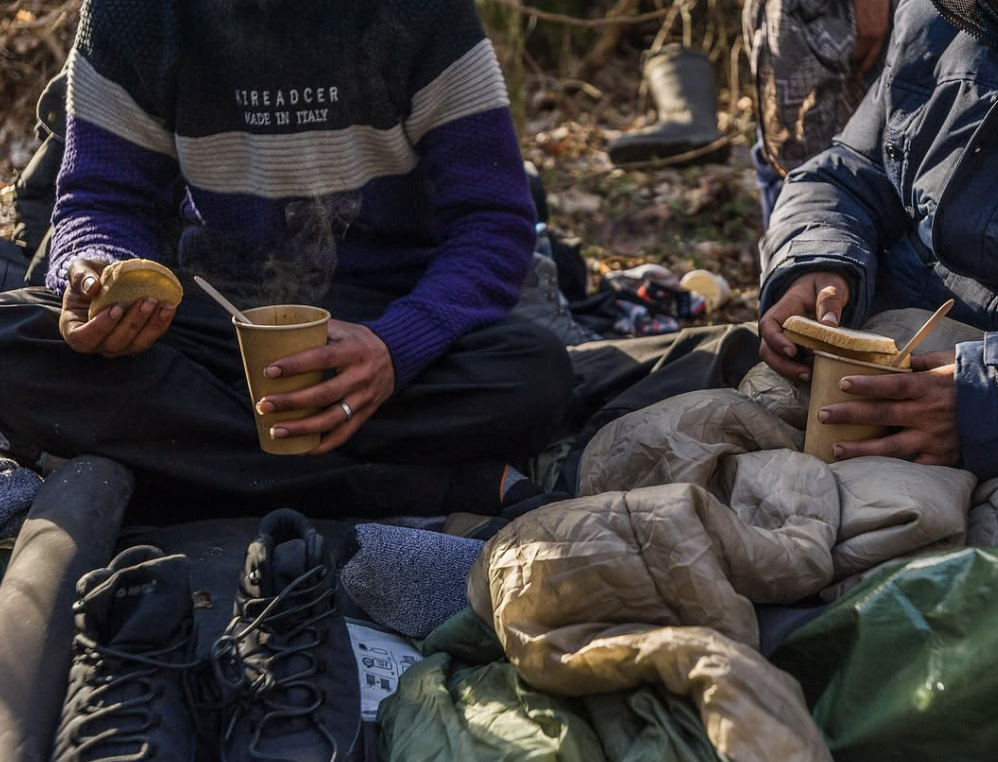 Migrants holding hot beverages and bread given to them.